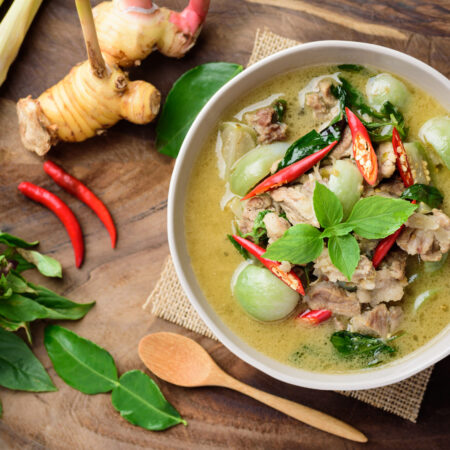 Thai food, Green curry with pork (Kang Keaw Wan) in a bowl with ingredients on wooden background, Top view
